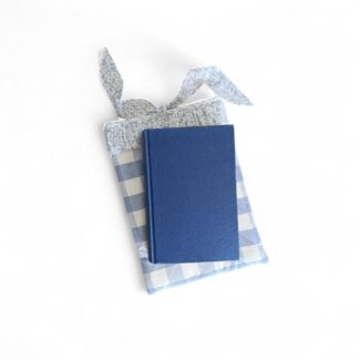 front-view-of-a-padded-blue-gingham-book-sleeve-with-a-decorative-floral-ruffled-edge-and-soft-fabric-tie-with-a-max-&-milo-brand-logo-stitched-onto-the-front-styled-with-hardcover-book