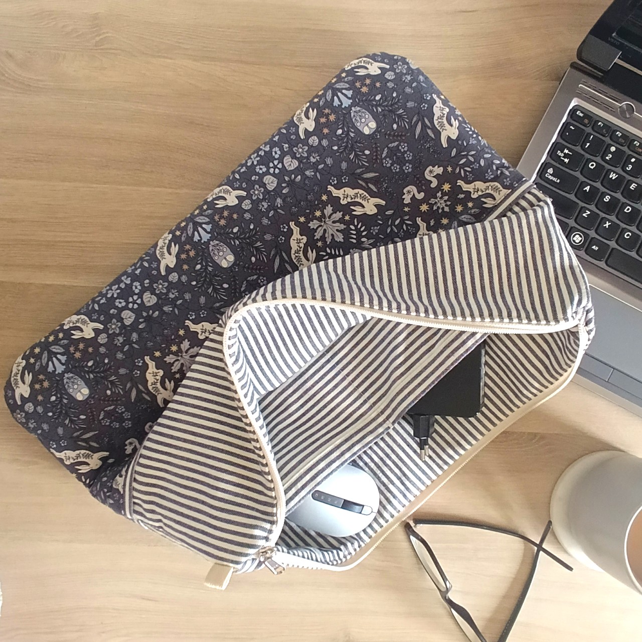 a-styled-view-of-a-navy-and-cream-laptop-sleeve-with-the-brand-name-max-&-milo-stitched-onto-the-front-of-the-sleeve-styled-with-a-laptop-mouse-charging-cable-coffee-cup-and-reading-glasses-on-a-desk-top