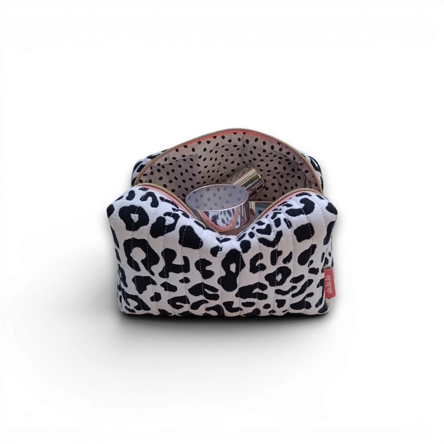 side-on-styled-view-of-a-black-and-white-quilted-boxy-bag-with-a-salmon-coloured-zipper-and-brand-lable